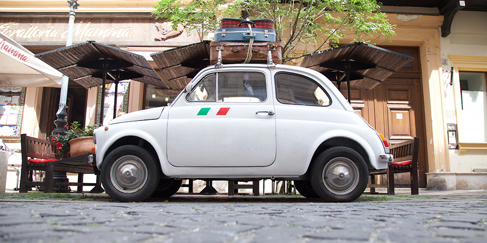 Carro Fiat 500 color blanco con equipaje en el techo, historico vehículo de la marca